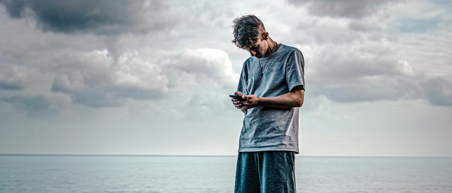 Man standing in front of the sea looking down at a phone